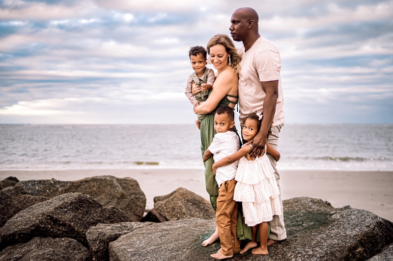 Family Photographer, a mom and dad stand with their three children on rocks near the sea