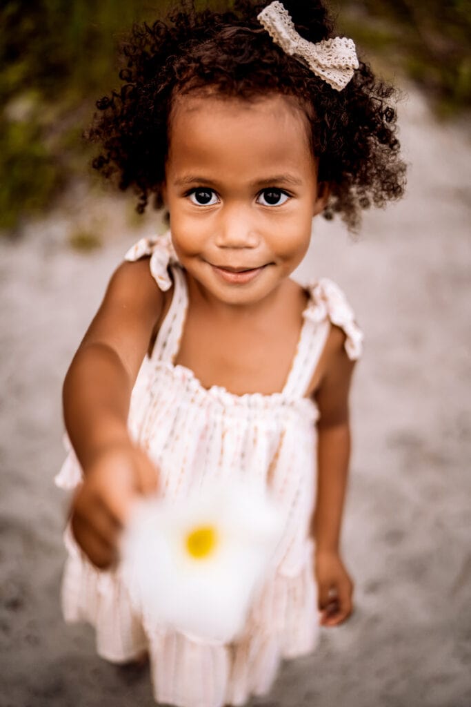 Family Photographer, a little girl holds a daisy and smiles outside