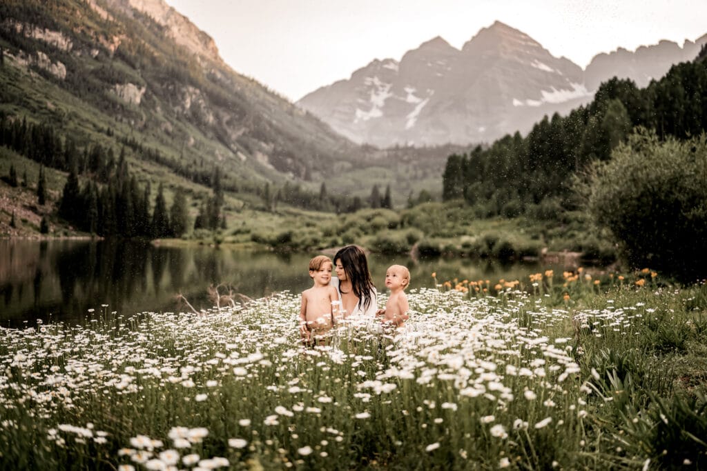 Family Photographer, a mother kneels in the wildflowers in mountain meadows with her two children