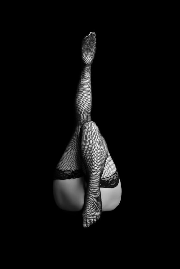 Boudoir Photographer, woman wears mesh stockings, laying down, one leg in the air
